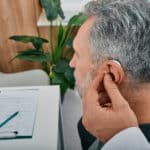 Audiologist Fits A Hearing Aid On Deafness Mature Man Ear While