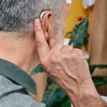 Senior Gray-haired Man Tunes His Hearing Aid Behind The Ear By P