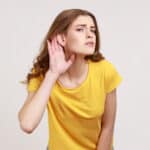 What. I cant hear. Portrait of girl in yellow T-shirt holding hand near ear